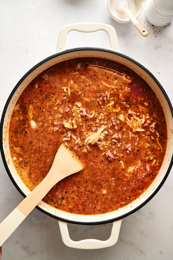 Sopa hirviendo en una olla con una cuchara de madera, mostrando queso fundido y fideos tiernos en un rico caldo de tomate.