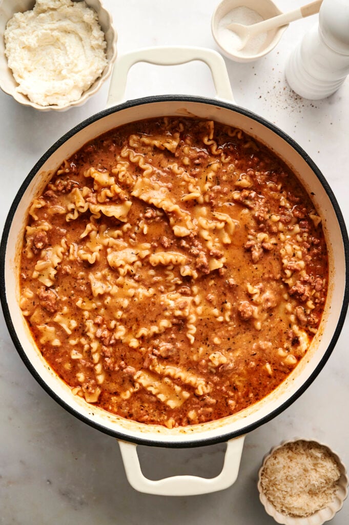 Sopa cremosa en una olla después de cocinar a fuego lento, con fideos tiernos y carne molida en un rico caldo de tomate, y queso ricotta al lado.
