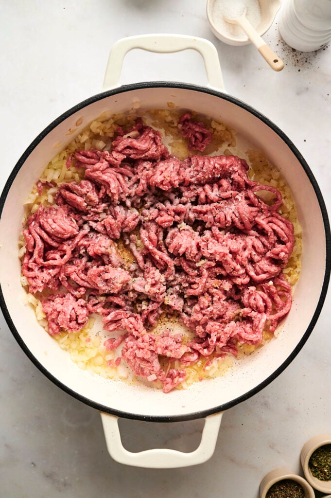 Carne molida siendo dorada con cebolla sofrita en una olla.