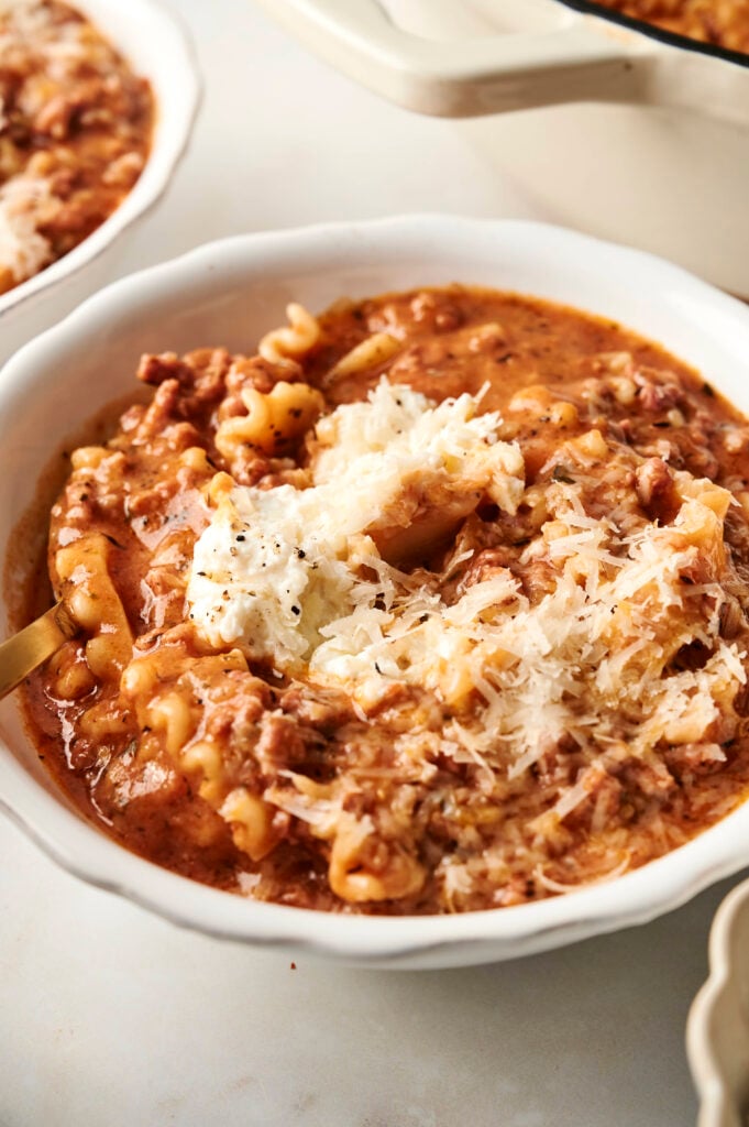 Tazón de sopa de lasaña abundante con fideos rizados, carne molida y una generosa cucharada de ricotta y parmesano.