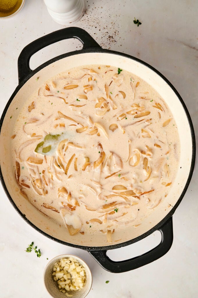 Cebollas caramelizadas cocinándose en una rica salsa de crema con hoja de laurel y tomillo, creando la base para el pollo cremoso con cebolla francesa.