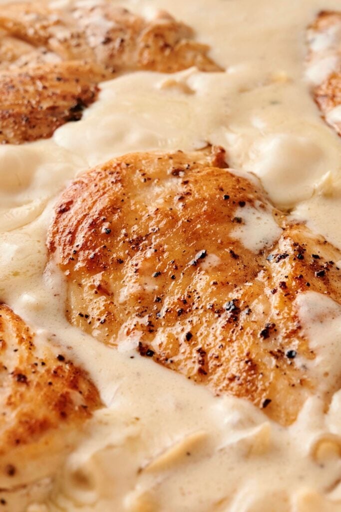 Primer plano de pechugas de pollo doradas cocinándose en una rica salsa de cebolla francesa cremosa con cebollas caramelizadas.