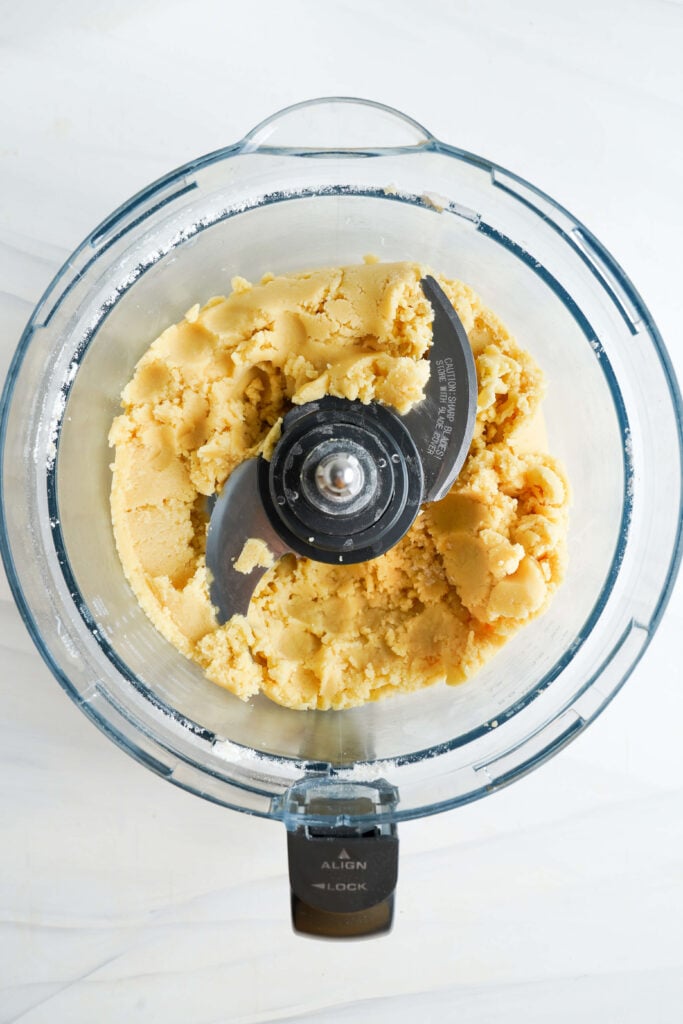 Masa de galleta de mantequilla en un procesador de alimentos, recién combinada y formando una textura suave y desmenuzada.