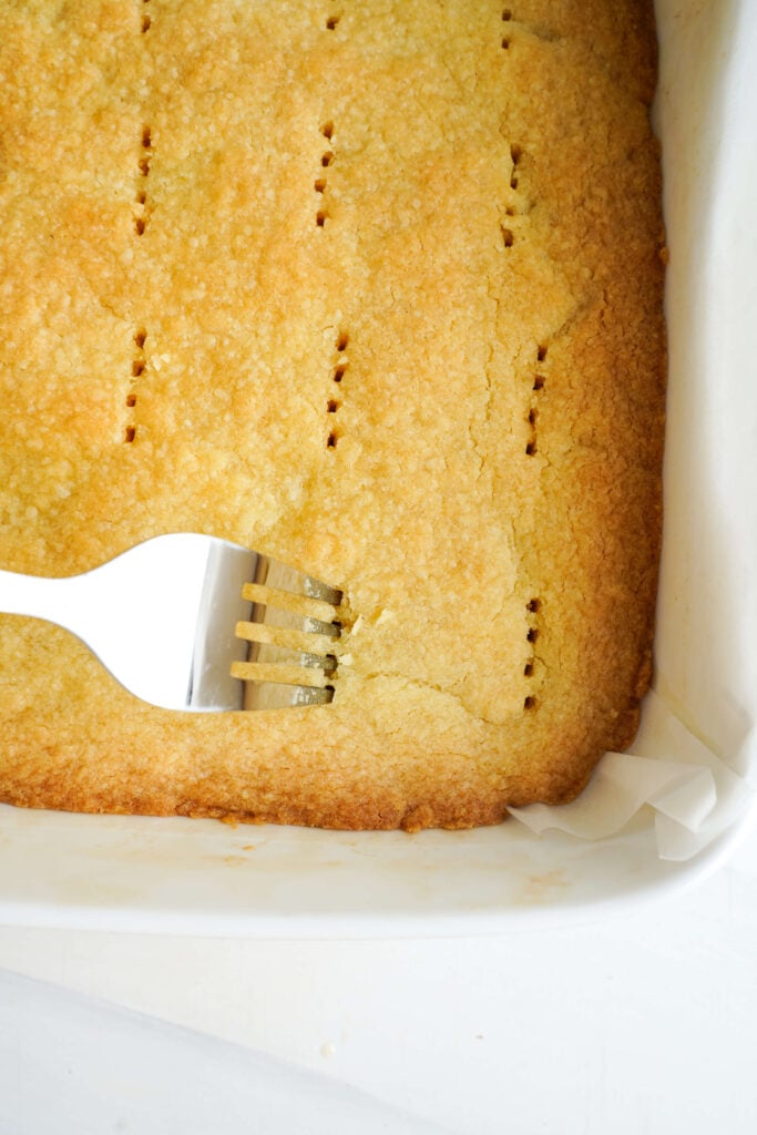 Usando un tenedor para hacer agujeros en la base de galleta recién horneada para ayudar al relleno de limón a adherirse.