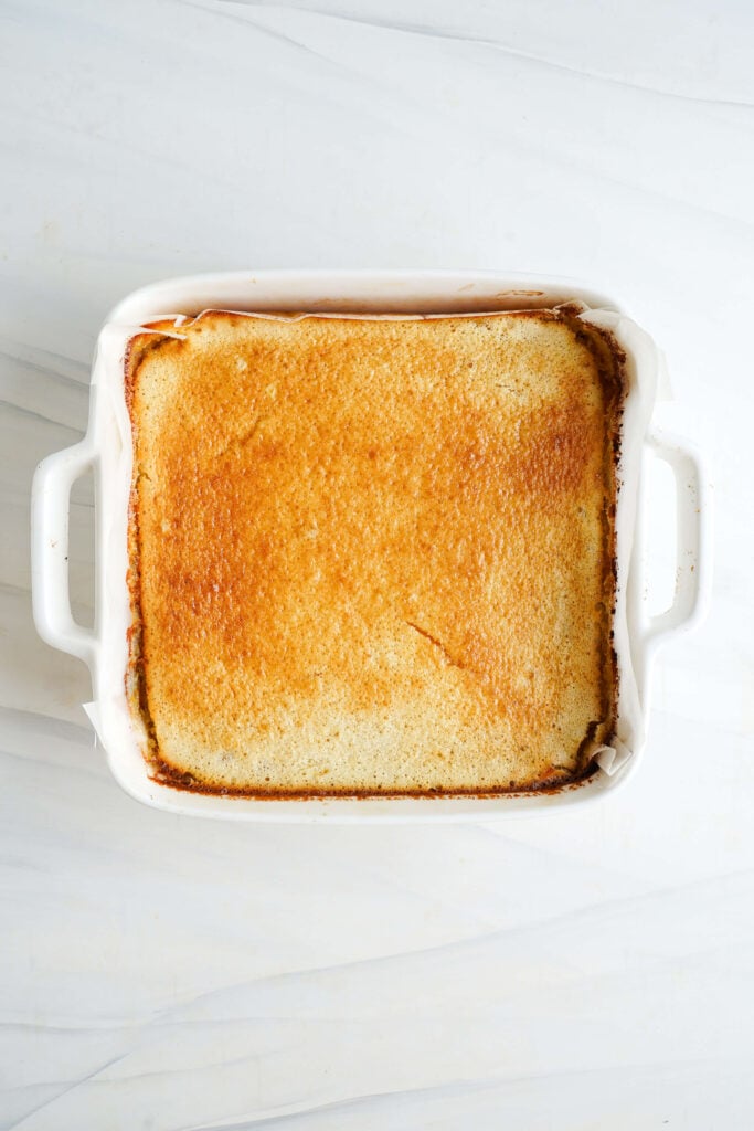 Barras de limón doradas recién salidas del horno en un molde blanco para hornear, mostrando una parte superior perfectamente cuajada y horneada uniformemente.