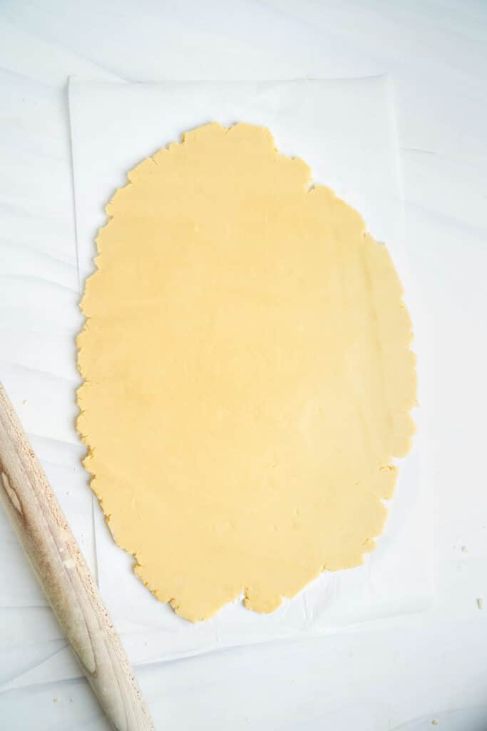 Masa de galleta de azúcar extendida sobre un trozo de papel pergamino. Rodillo al lado.