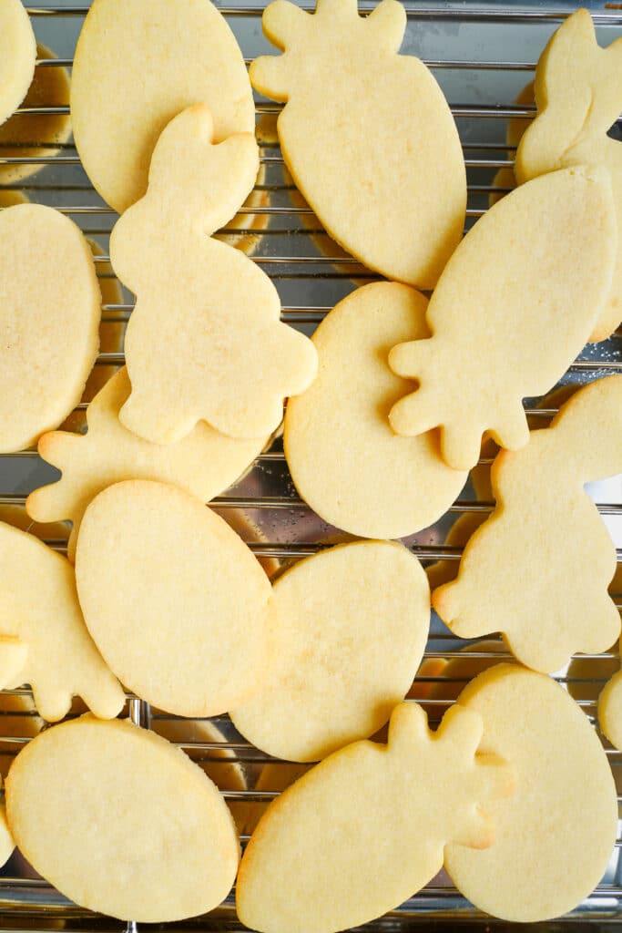Galletas de azúcar de Pascua recién horneadas en formas de conejo, zanahoria y huevo enfriándose sobre una rejilla.
