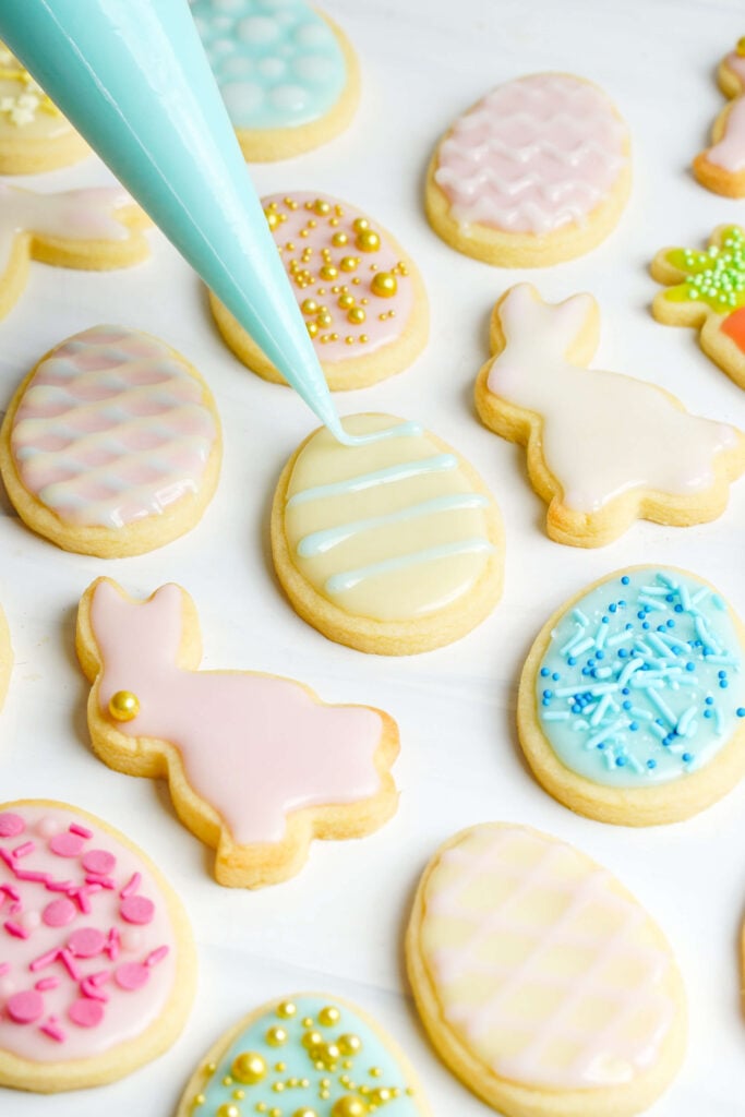 Decorando galletas de azúcar de Pascua con glaseado azul claro rodeadas de galletas en formas de conejo, huevo y zanahoria.