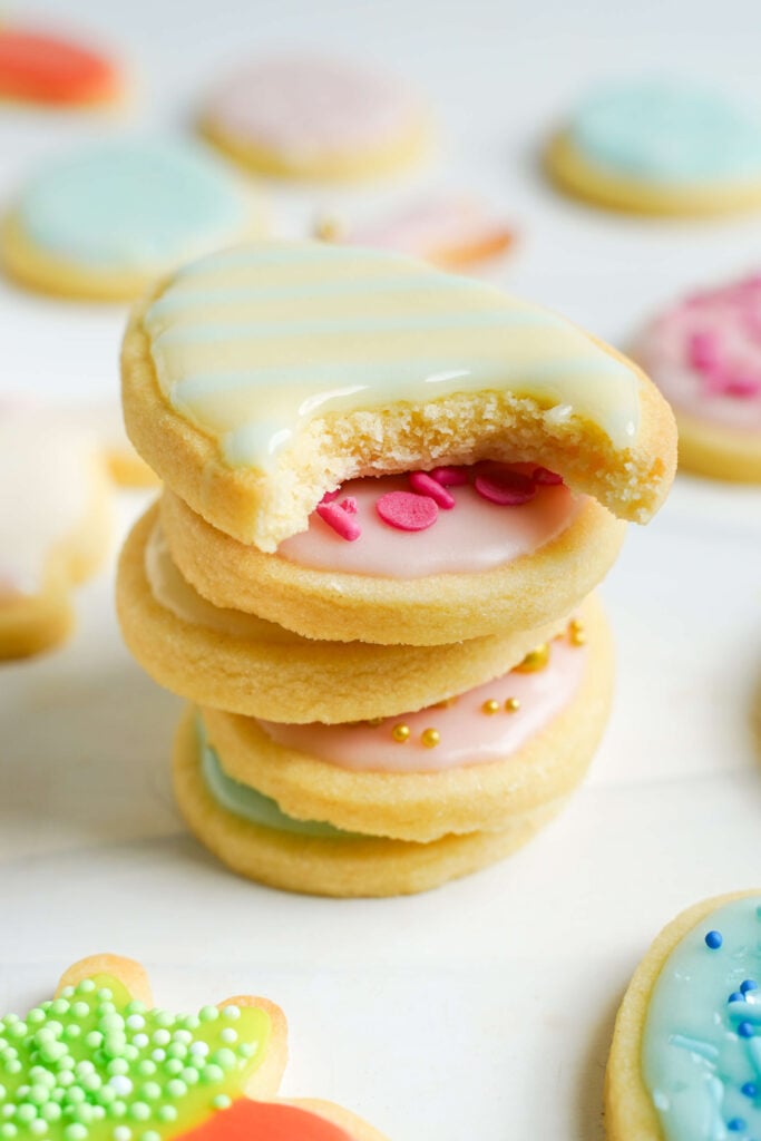 Montón de galletas de azúcar de Pascua decoradas con glaseado pastel y chispas, con la galleta de arriba mostrando un mordisco para revelar su textura suave y tierna.