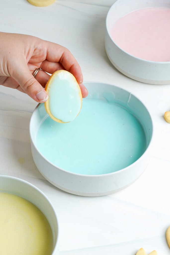 Galleta de azúcar de Pascua recién sumergida siendo levantada de un tazón de glaseado azul pastel con un recubrimiento suave.