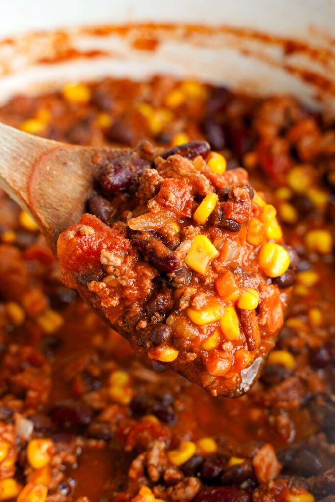 Chili con carne, bacon, frijoles, maíz y una mezcla de especias, servido en una cuchara de madera sacada de un horno de hierro fundido.