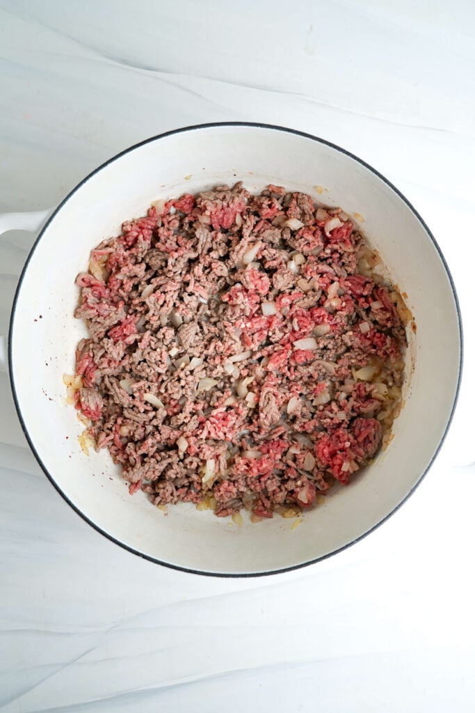 Carne molida dorándose con cebollas en una olla de hierro fundido.