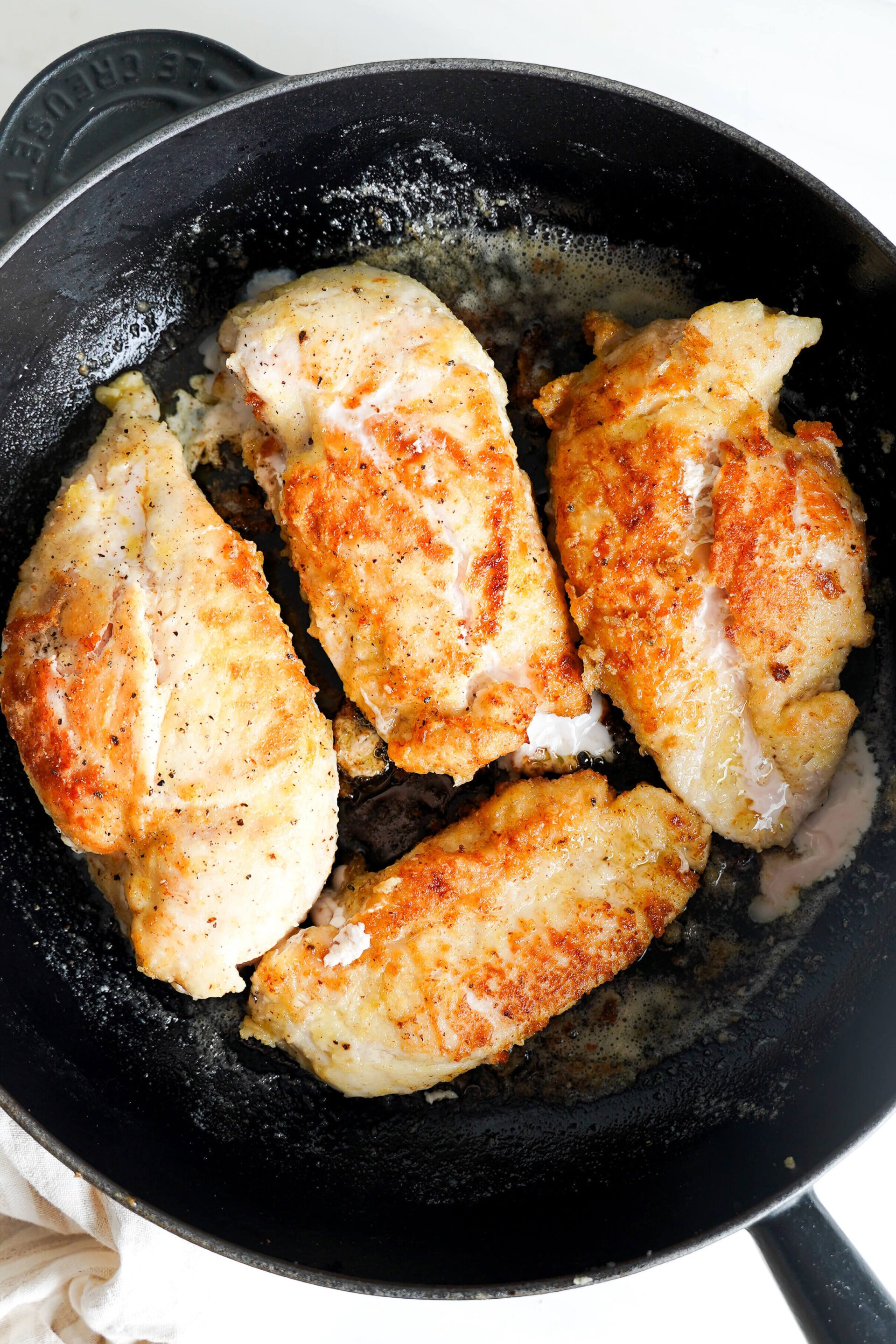 Pechugas de pollo sellándose en una sartén con mantequilla, desarrollando una costra dorada.