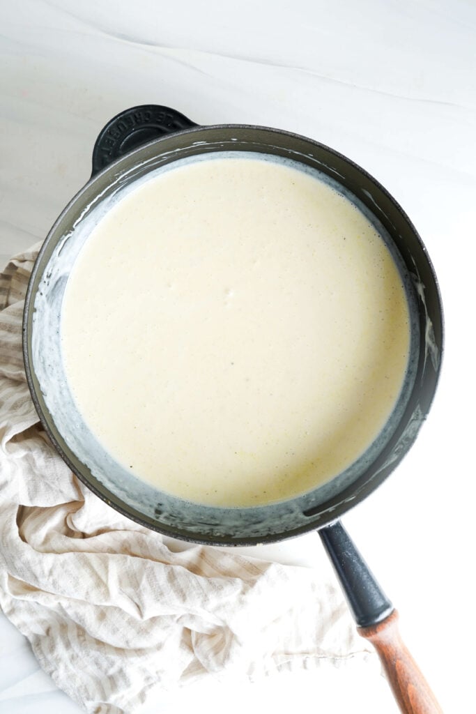 Primer plano de salsa cremosa al limón hirviendo en una sartén negra sobre una superficie blanca.