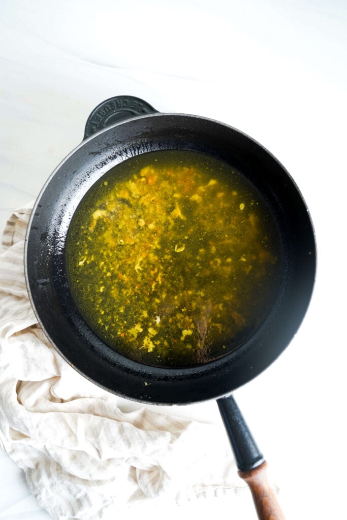 Mezcla de jugo de limón, ralladura, caldo y ajo chisporroteando en una sartén antes de agregar la crema.
