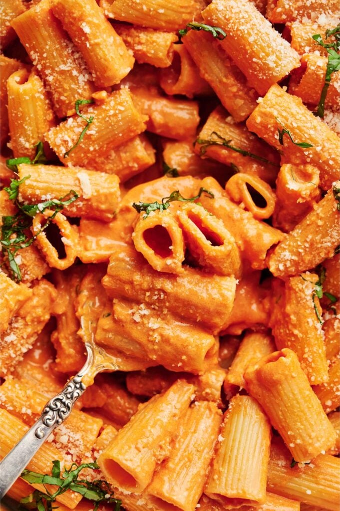 Pasta rigatoni cremosa alla vodka cubierta con parmesano rallado y albahaca fresca, mostrada de cerca con una cuchara vintage