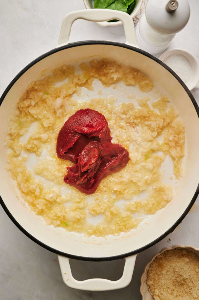 Pasta de tomate añadida al ajo y cebolla sofritos en una sartén blanca