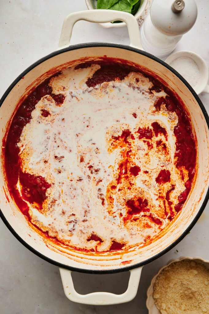 Crema espesa vertida en la rica salsa de tomate antes de mezclar