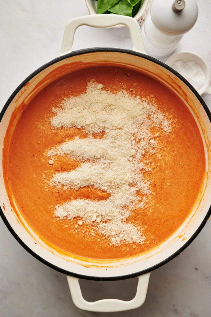 Queso parmesano rallado fresco espolvoreado sobre salsa cremosa de tomate y vodka en una sartén blanca, listo para mezclar