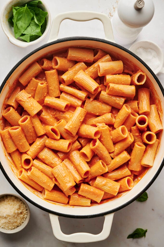 Gran olla de pasta rigatoni uniformemente cubierta con salsa de vodka casera, justo antes de adornar con albahaca y queso