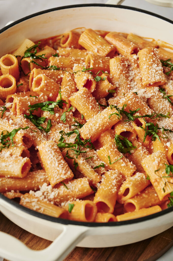 Rigatoni mezclada en salsa cremosa de vodka, adornada con parmesano recién rallado y albahaca en rodajas finas, lista para servir