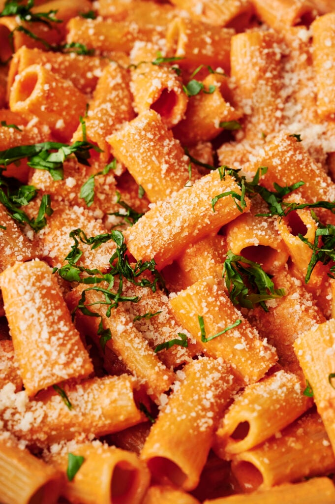 Pasta rigatoni cremosa alla vodka cubierta con parmesano recién rallado y albahaca en rodajas finas, mostrada de cerca para resaltar su textura
