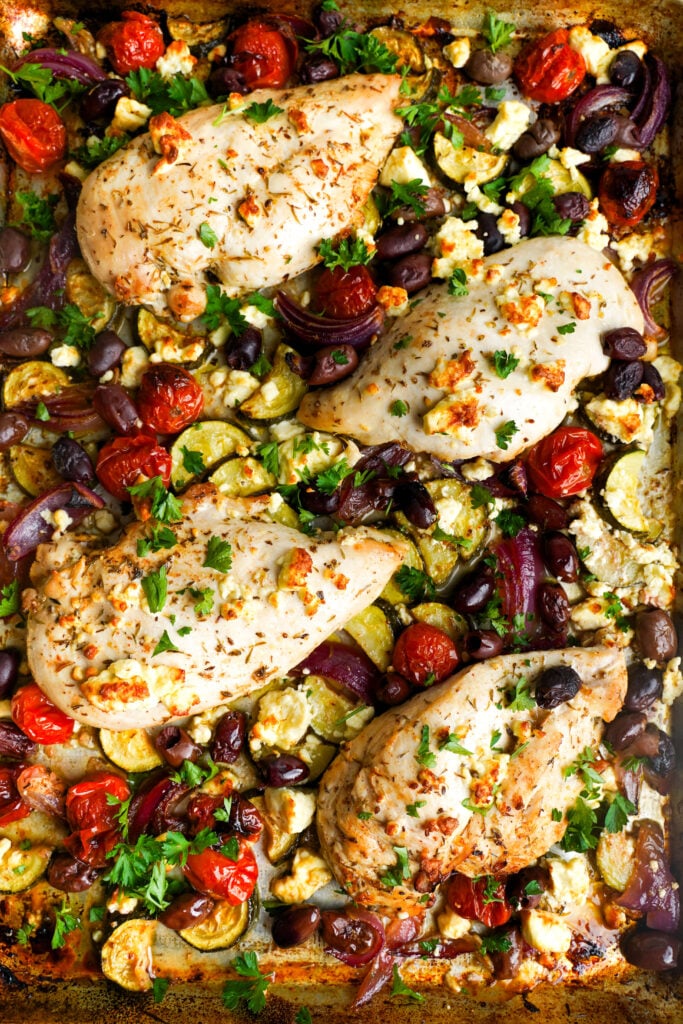 Pechugas de pollo asadas con verduras, aceitunas y feta en una bandeja después de hornear