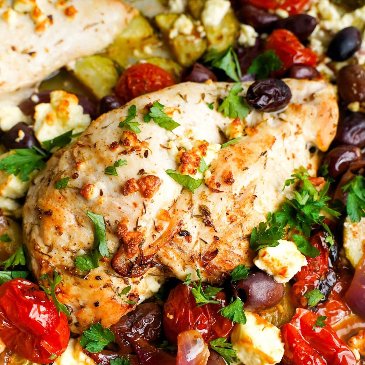 Close-up of Greek sheet pan chicken with roasted cherry tomatoes, olives, red onion, and crumbled feta