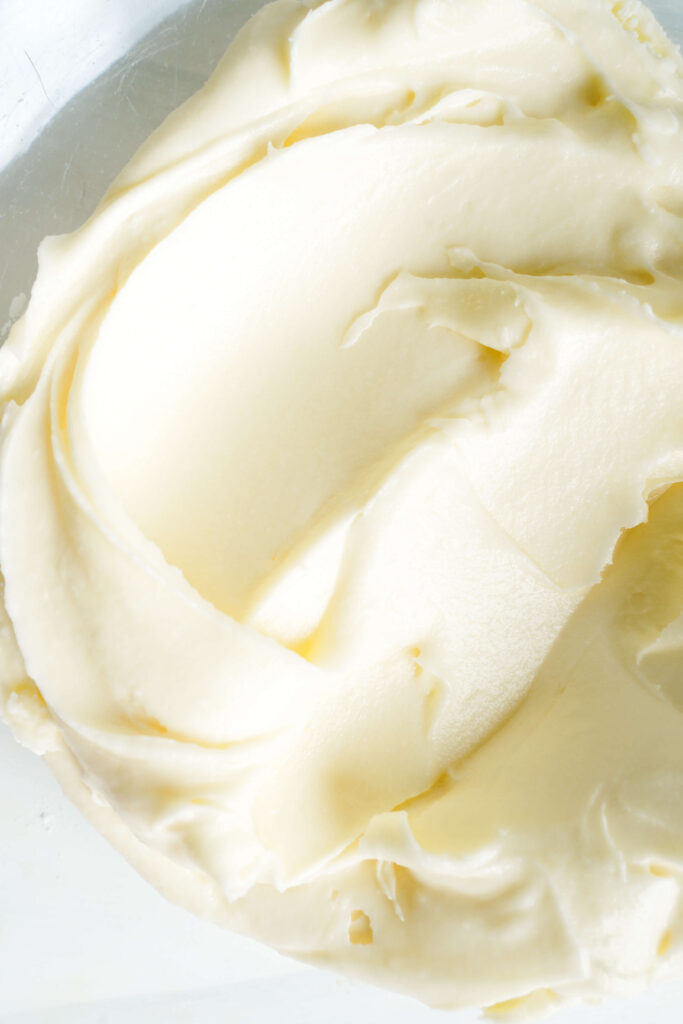 Glaseado de queso crema casero suave y cremoso mezclado en un tazón, listo para esparcir sobre el pastel de plátano