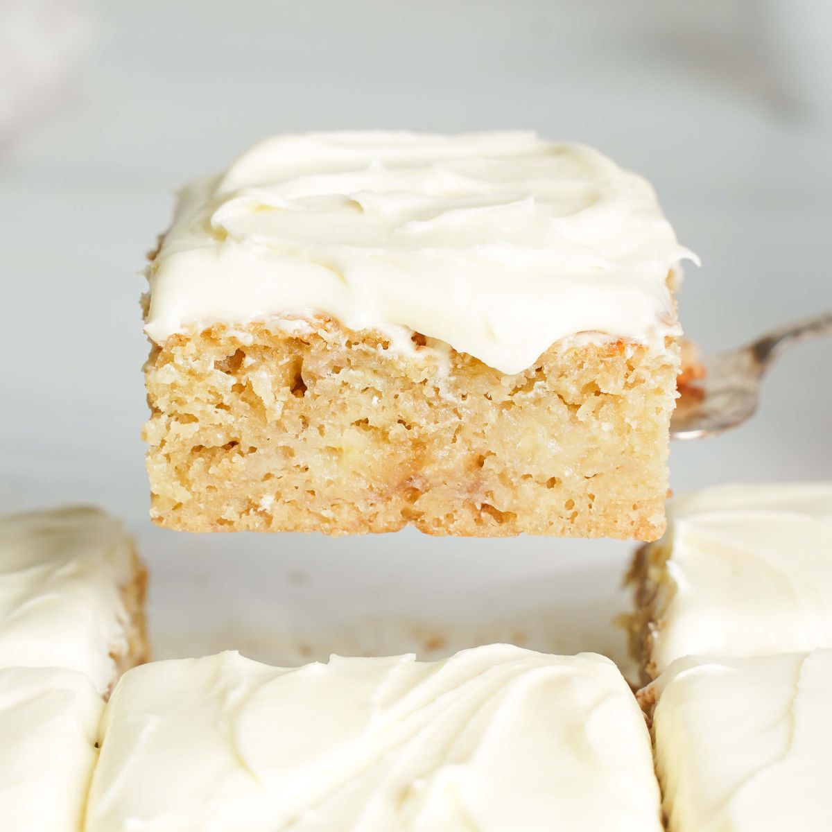 Primer plano de una rebanada de pastel de plátano húmedo con glaseado de queso crema levantada de un molde