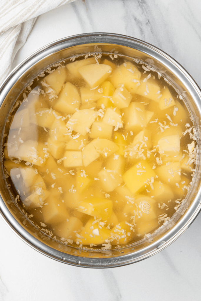 Patatas Yukon Gold en cubos y ajo picado en una olla de agua antes de hervir.