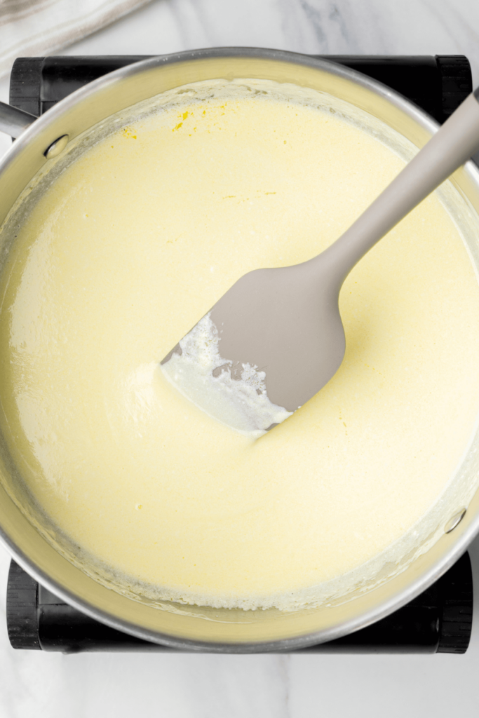 Mezcla de mantequilla y crema derretida siendo removida con una espátula gris en una cacerola.