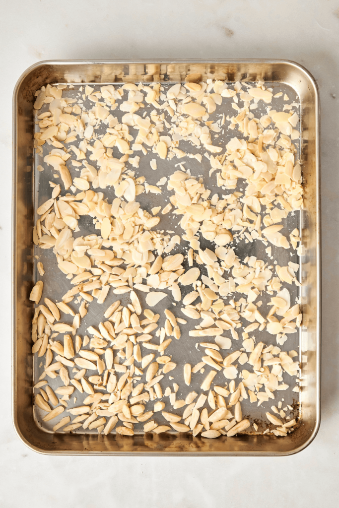 Almendras fileteadas y laminadas distribuidas uniformemente en una bandeja de hornear metálica.