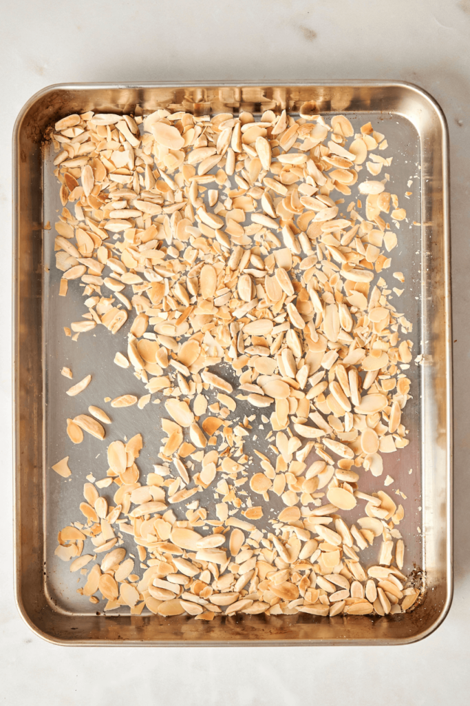Almendras fileteadas y laminadas tostadas esparcidas en una bandeja de hornear metálica.