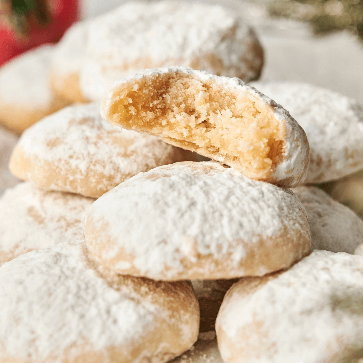 Un montón de galletas de almendra en forma de nieve espolvoreadas con azúcar en polvo, con una galleta rota por la mitad para mostrar su interior suave y mantecoso.