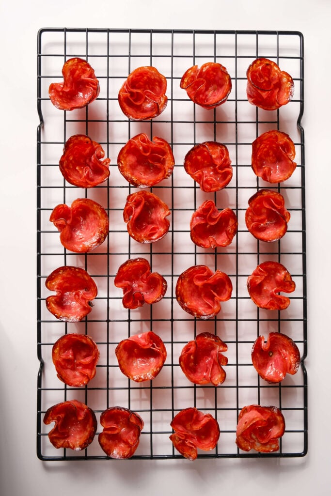 Tazas de salami horneadas y crujientes dispuestas sobre una rejilla de enfriamiento, listas para ser rellenas para un aperitivo.