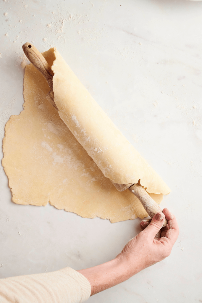 Masa de tarta envuelta alrededor de un rodillo, lista para ser transferida a un molde para tarta.