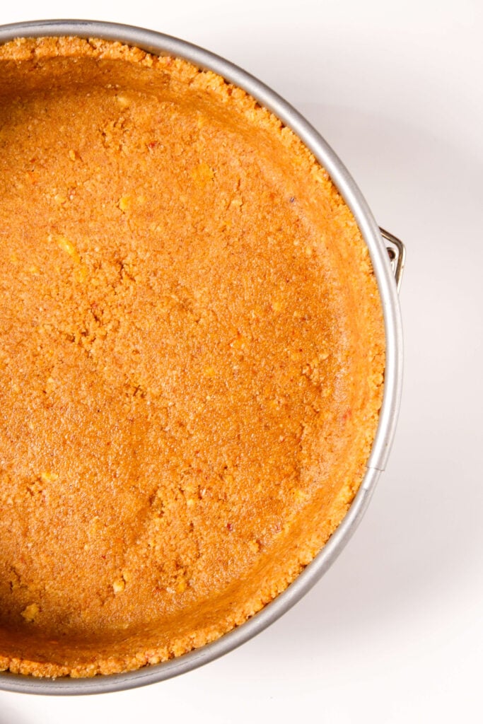 Primer plano de una base de galleta graham y nueces perfectamente presionada en un molde desmontable, lista para el relleno del cheesecake de calabaza.