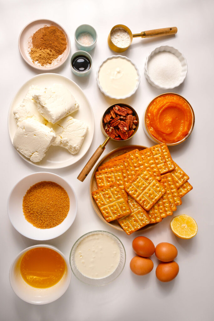Una vista desde arriba de todos los ingredientes necesarios para un cheesecake de calabaza, incluyendo queso crema, puré de calabaza, azúcar moreno y especias.