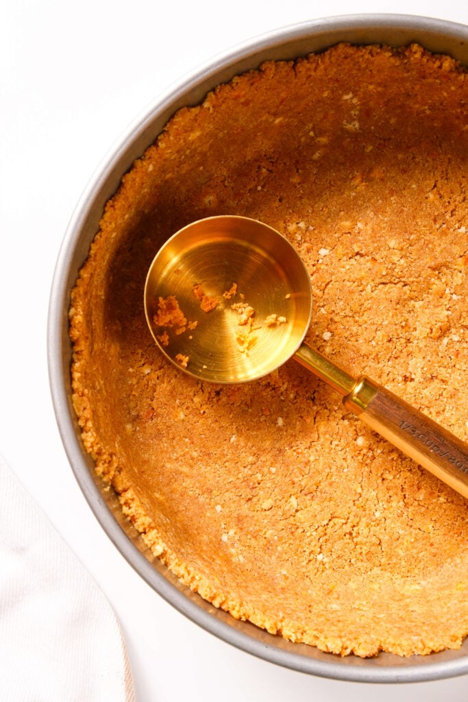 Un molde desmontable con la base de galleta graham presionada uniformemente para un cheesecake de calabaza.