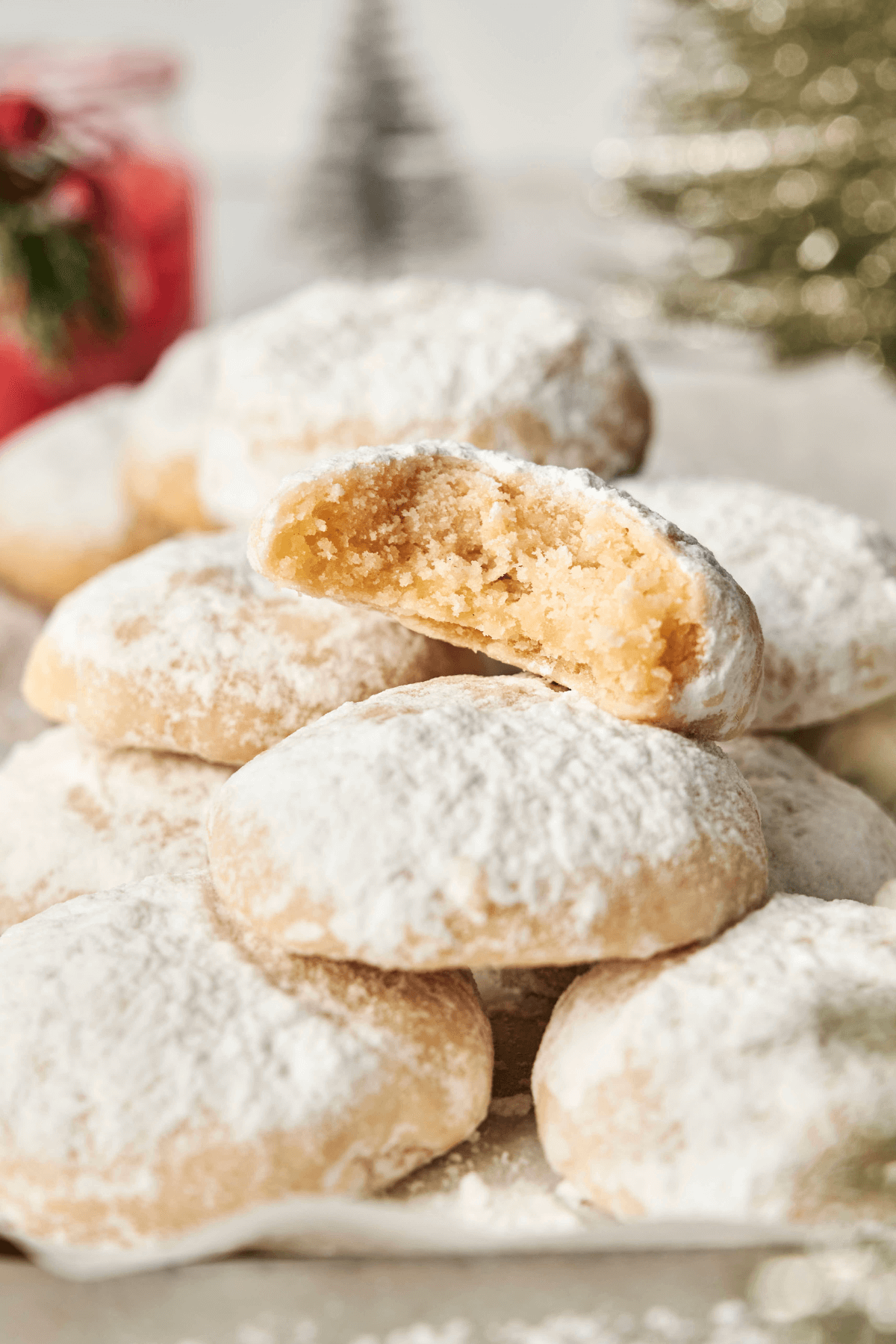 Un montón de galletas de almendra en forma de nieve espolvoreadas con azúcar en polvo, con una galleta rota por la mitad para mostrar su interior suave y mantecoso.