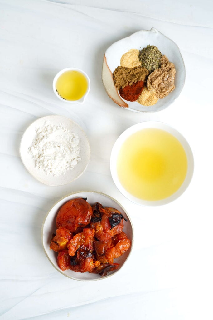 Todos los ingredientes para la salsa de enchiladas medidos en pequeños tazones sobre una superficie blanca