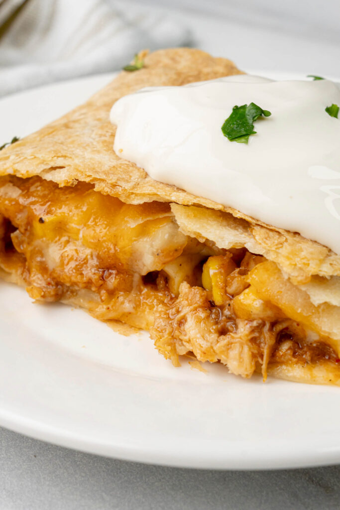 Primer plano de una quesadilla de pollo con queso derretido y pollo desmenuzado, coronada con una cucharada de crema agria y cilantro fresco