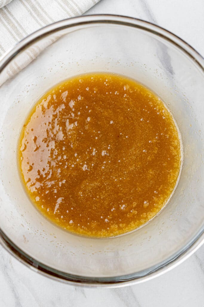 Ingredientes húmedos batidos en un tazón de vidrio, incluyendo aceite, azúcares, huevos, vainilla y leche, mezclados hasta que estén suaves y brillantes.