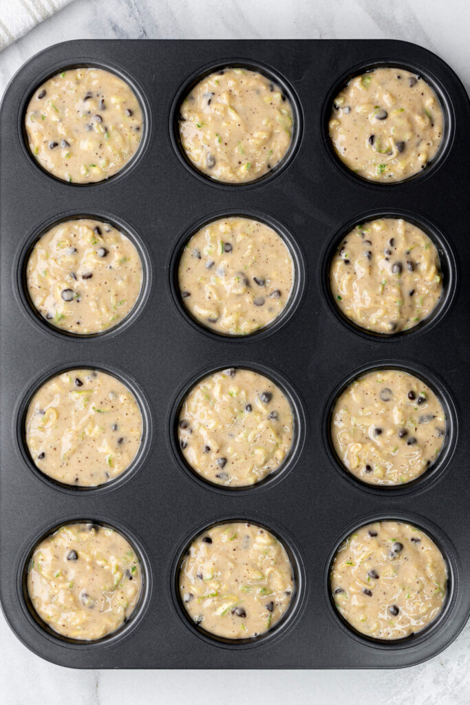 Molde para muffins lleno con masa de muffin de calabacín y chispas de chocolate lista para hornear.