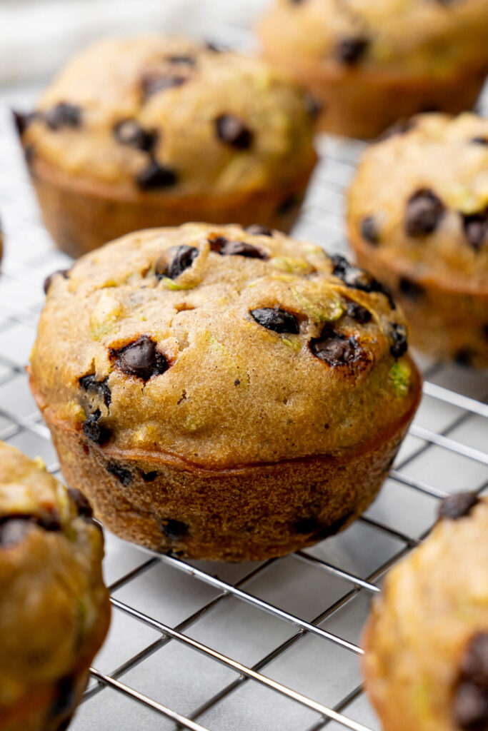 Primer plano de muffins de calabacín con chispas de chocolate recién horneados enfriándose en una rejilla, mostrando bordes dorados y chispas de chocolate derretidas.