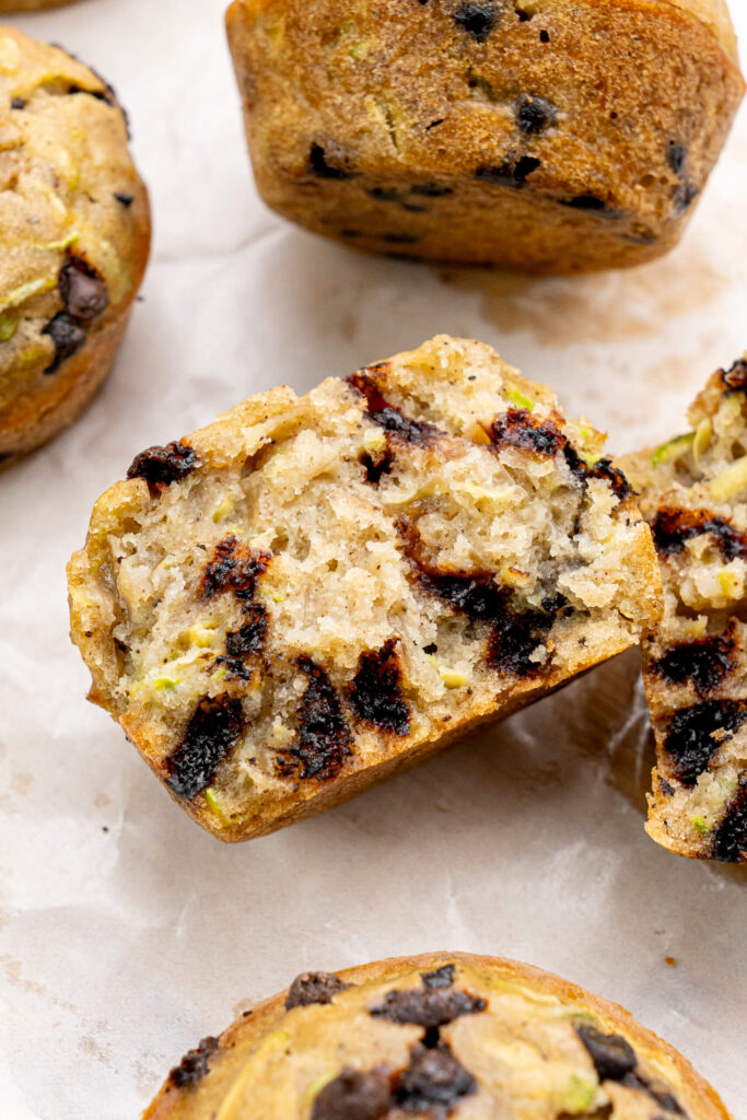 Primer plano de un muffin de calabacín con chispas de chocolate cortado por la mitad mostrando un interior suave y húmedo con chispas de chocolate derretidas y motas de calabacín verde.