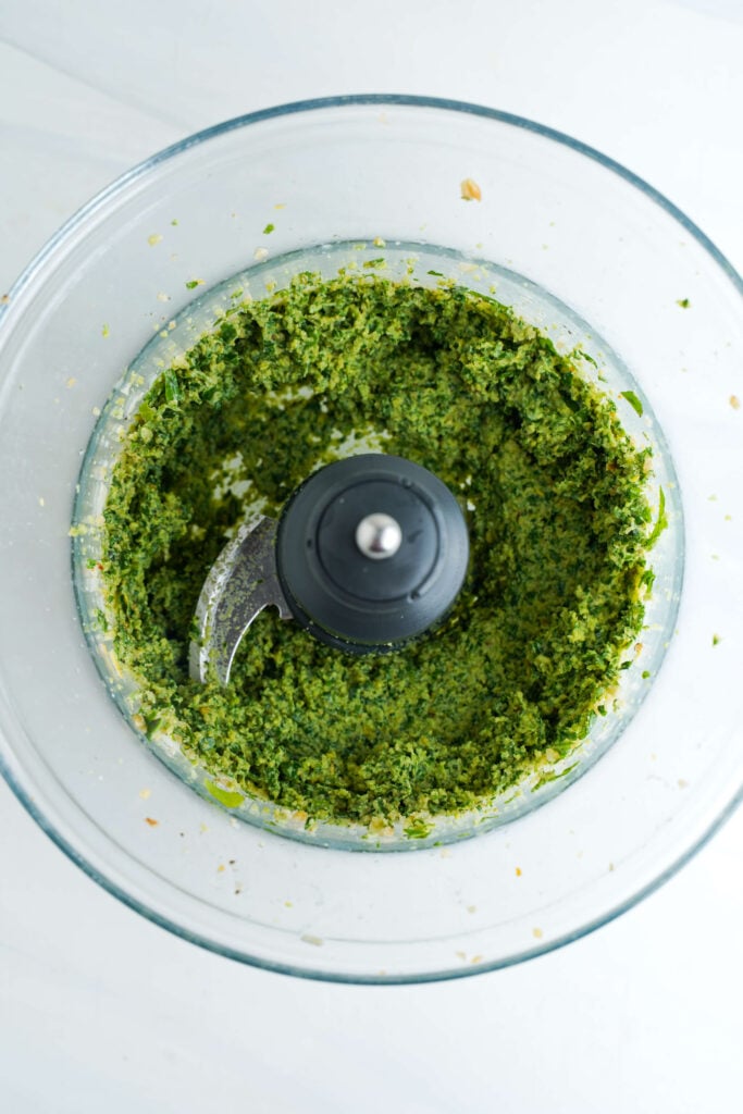 Albahaca fresca procesada en la base de ajo y piñón en un procesador de alimentos.